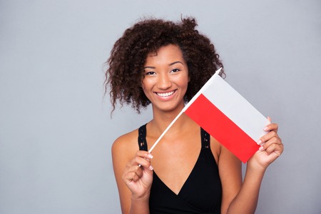 Portrait of a happy afro american woman holding Poland flag over gray background and looking at cameraの写真素材