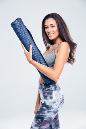 Portrait of a happy fitness woman holding yoga mat isolated on a white backgroundの写真素材