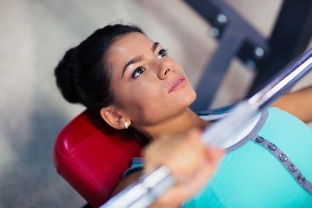 Young sports woman workout with barbell on the bench in fitness gym