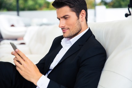 Handsome man sitting at restaurant and using smartphoneの写真素材