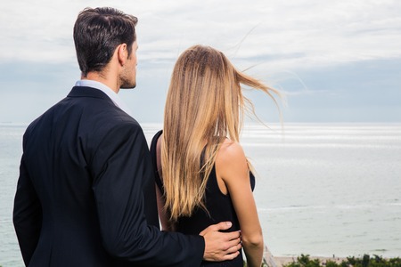 Back view portrait of romantic couple standing outdoors and looking at seaの写真素材