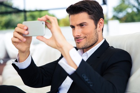 Confident businessman making selfie photo on smartphone in restaurantの写真素材