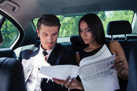 Businessman and businesswoman reading documents in car