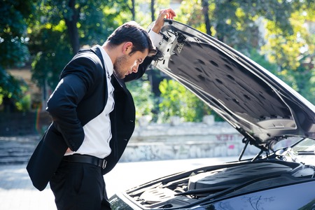 Man standing near broken car with open hoodの写真素材