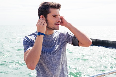 Sports man standing with headphones near sea outdoors and looking awayの写真素材