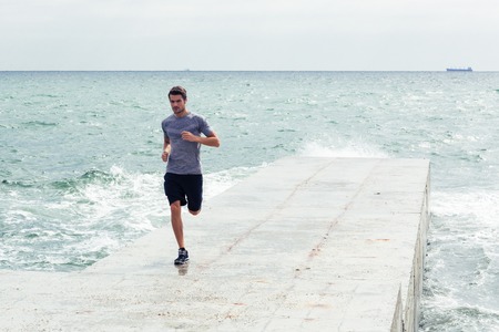 Full length portrait of a sports man running at the beach outdoorsの写真素材