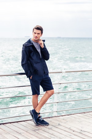 Portrait of a handsome sports man standing outdoors in the morning with sea on background