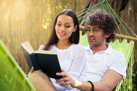 Portrait of a smiling couple reading book together outdoors on hammokの写真素材