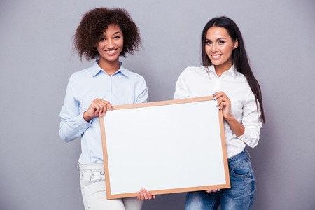 Portrait of a two girls holding blank board over gray backgroundの写真素材