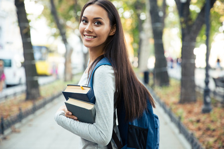 Portrait of a happy female student holding books and looking at camera outdoorsの写真素材