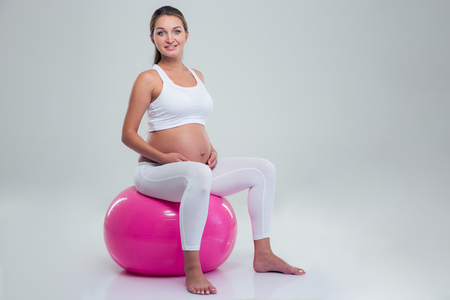 Portrait of a pregnant woman sitting on a fitness ball isolated on a white backgroundの写真素材