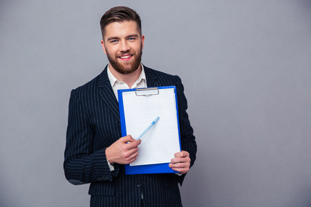 Portrait of a smiling businessman showing blank clipboard over gray backgroundの写真素材