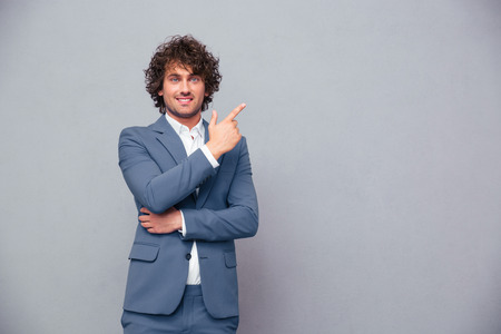Portrait of a smiling businessman pointing finger away over gray background and looking at cameraの写真素材