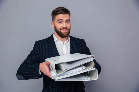 Portrait of a happy businessman holding folders over gray backgroundの写真素材