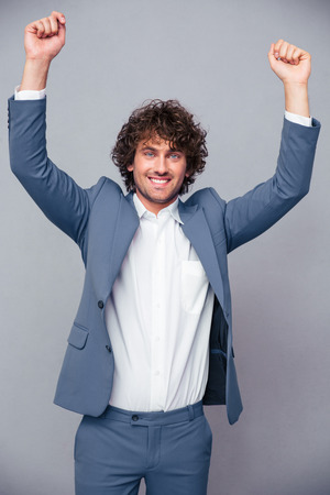 Portrait of a happy businessman celebrating his success with raised hands up over gray backgroundの写真素材