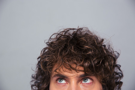 Cropped image of a man with curly hair looking up at copyspace over gray backgroundの写真素材