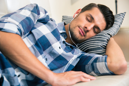 Portrait of a handsome man sleeping on the sofa with headphones at homeの写真素材