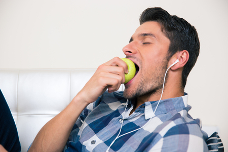 Portrait of a handsome man eating apple on the sofaの写真素材