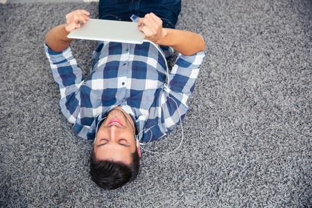 Portrait of a happy man lying on the floor with tablet computer at homeの写真素材
