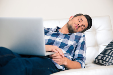 Portrait of a young man sleeping with laptop on the sofa at home