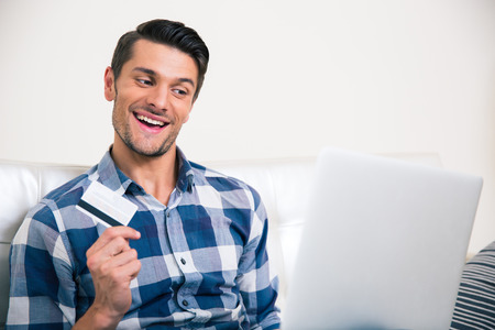 Portrait of a cheerful man holding bank card and looking at laptopの写真素材