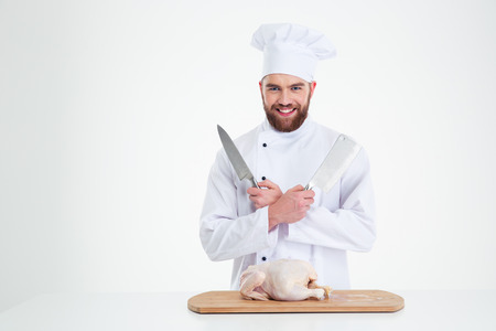 Portrait of a happy male chef cook standing with knifes and chicken on the table isolated on a white backgroundの写真素材