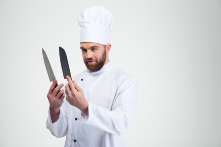 Portrait of a young chef cook holding and looking on knifes isolated on a white backgroundの写真素材