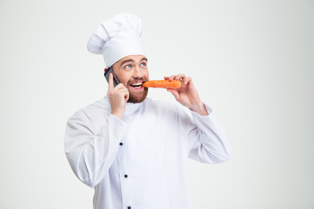 Portrait of a male chef cook talking on the phone and eating carrot isolated on a white backgroundの写真素材