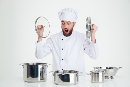 Portrait of a funny male chef cook sitting at the table with dishes isolated on a white backgroundの写真素材