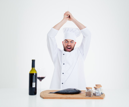 Portrait of angry male chef cook cutting fish isolated on a white backgroundの写真素材