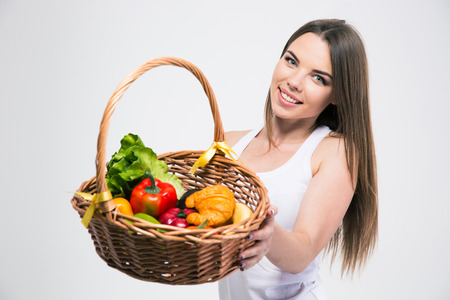 Portrait of a smiling cute girl giving basket with fruits at the camera isolated on a white backgroundの写真素材