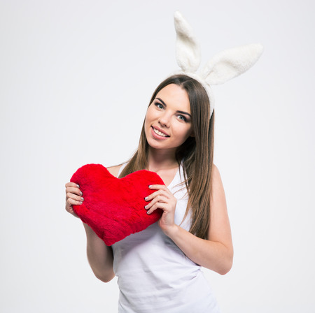Portrait of a smiling cute girl with rabbit ears holding heart isolated on a white backgroundの写真素材