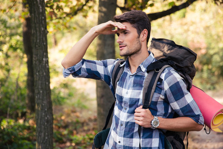 Portrait of a young man with marching backpack looking away in forestの写真素材
