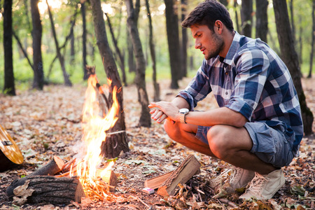 Portrait of a handsome man sitting near bonfire in the forest
