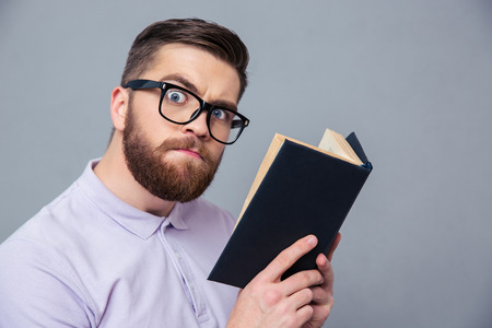 Portrait of a serious casual man holding book over gray background and looking at cameraの写真素材