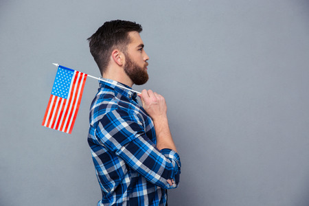 Side view portrait of a casual man holding USA flag over gray backgroundの写真素材