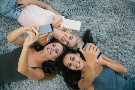 Top view portrait of a three girlfriends using smartphones on the carpet at home