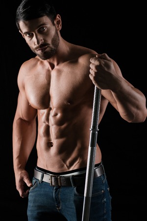 Portrait of a handsome man with muscular body holding barbell on black backgroundの写真素材