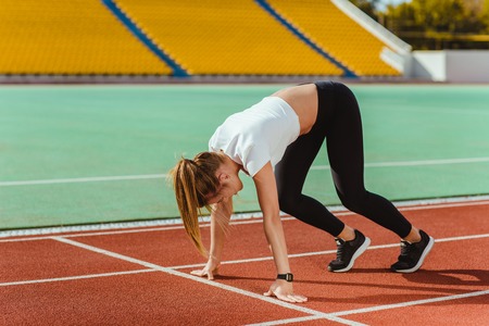 Portrait of a female runner in start position at outdoor stadium