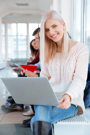 Portrait of a happy female student sitting with laptop at university hallの写真素材