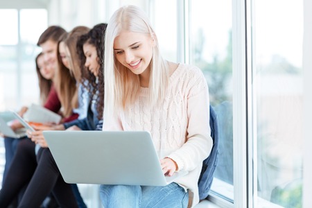 Portrait of a smiling students using laptop in university hallの写真素材
