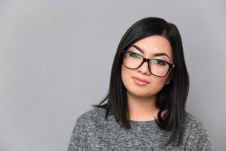 Portrait of a beautiful woman in glasses looking at camera over gray backgroundの写真素材