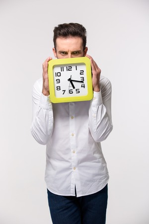 Portrait of a businessman covering his face with wall clock isolated on a white backgroundの写真素材