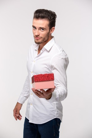 Portrait of a handsome man givinggift box on camera isolated on a white backgroundの写真素材