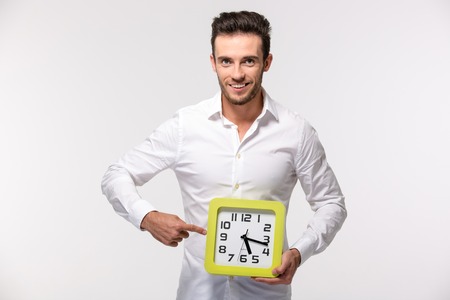 Portrait of a smiling businessman in shirt pointing finger on wall clock isolated on a white backgroundの写真素材