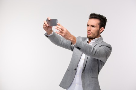 Portrait of a young businessman making selfie photo on smartphone isolated on a white backgroundの写真素材