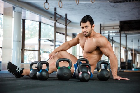 Portrait of a handsome man siting on the floor with kettle balls in fitness gym and looking at cameraの写真素材
