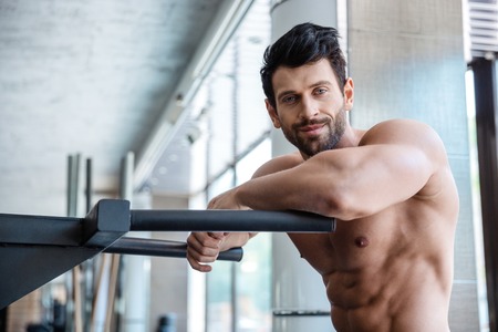 Portrait of a handsome man resting near parallel bars in fitness gym and looking at cameraの写真素材