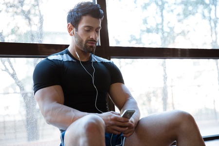 Athletic man wearing black t-shirt listening to music sitting on windowcillの写真素材