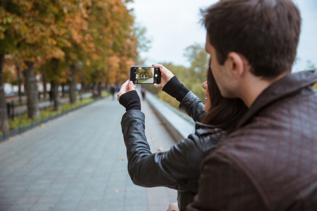 Portrait of a young couple making photo on smartphone of autumn parkの写真素材